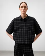 Camisa de manga corta con cuello solapa y bolsillo de plastrón en el pecho. Presenta un tejido seersucker negro con un patrón de cuadros finos en tonos claros.