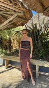 Pollera larga de microtul color marrón, con diseño de transparencias, detalle de fruncido lateral y volados verticales a lo largo de la abertura frontal.