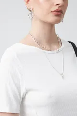 Remera de manga corta color beige claro, confeccionada en tejido acanalado elástico, con cuello redondo.