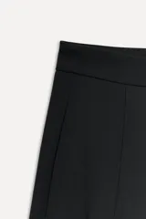 Pantalón negro de tiro bajo confeccionado en lana 100%, con bolsillos laterales ocultos y bolsillos de vivo en la espalda. Tiene pierna ancha y cierre frontal con cremallera, botón interior y ganchos metálicos.