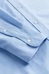 Camisa celeste de algodón Oxford, de corte relajado, con cuello clásico, botones frontales, canesú con trabilla en la espalda, hombros caídos, mangas largas con puños sencillos y bajo redondeado con espalda algo más larga.