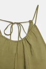 Vestido midi de color verde oliva, con cuello redondo y tirantes finos ajustables mediante un lazo en la espalda. El tejido presenta un acabado arrugado o texturizado.