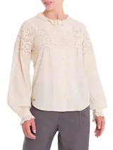 Blusa beige de algodón orgánico con cuello alto y detalles de broderie en la parte superior.