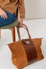 Bolso de viaje en gamuza azul, con asas de cuero y amplio compartimento principal.