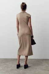Vestido midi color beige con cuello polo, escote en pico, manga sisa caída y detalle de drapeado lateral. Cierre frontal con botones metálicos en relieve.
