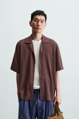 Camisa de manga corta con cuello bowling y calce relajado. Presenta un tejido con textura estructurada y efecto lavado, con cierre frontal de botones al tono.