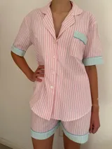 Conjunto de pijama de algodón a rayas verticales rosas y blancas, con detalles en celeste. Incluye camisa de manga corta con botones y bolsillo en el pecho, y shorts con cintura elástica.