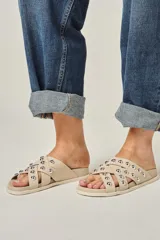 Sandalias color beige de cuero vacuno, con tiras entrelazadas y tachas redondas plateadas.