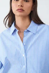 Camisa celeste a rayas verticales blancas, de popelina asimétrica y manga larga.