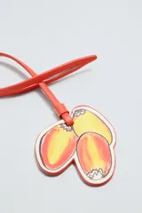 Llavero de cuero con diseño de tres frutas: dos mitades de durazno y una ciruela, con cordón de cuero naranja para colgar. Accesorio de la colección Filipe Jardim x Zara.