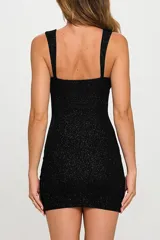 Vestido corto negro con glitter, de corte ajustado, breteles finos y tajo en la pierna.