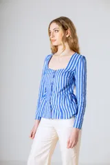Blusa de mangas largas con puños abotonados, de corte recto con peplum en la cintura y escote cuadrado. Diseño a rayas verticales azules y blancas con cierre frontal abotonado.