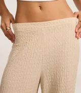 Pantalón largo color beige, de poliéster texturizado, con cintura elástica y bolsillos laterales.