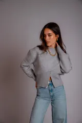 Buzo gris de punto con cuello redondo, mangas largas abullonadas y cierre frontal asimétrico.