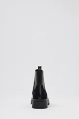 Bota negra de caña corta con paneles laterales elásticos, suela track y detalles en gamuza negra y cuero marrón en la parte trasera.