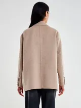 Chaqueta de lana color beige, de corte recto y levemente oversize, con solapa clásica y cierre de dos botones negros. Posee bolsillos con tapa a la altura de la cadera y un bolsillo de ojal en el pecho.