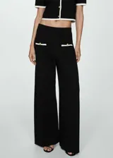 Pantalón negro de punto fino con diseño recto y largo, tiro medio, cintura elástica, ribetes en contraste y bolsillos de ribete delanteros con botones decorativos.