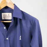 Camisa azul marino de algodón con cuello italiano, manga larga con puños abotonados y cierre frontal con botones blancos. Tiene un logo bordado en blanco en el pecho.