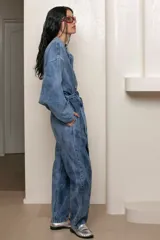 Mameluco de jean celeste con efecto nevado vintage, corte holgado, cuello mao, cierre frontal con botones y cinturón de lazo.