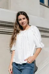 Blusa blanca de algodón con mangas 3/4 y escote redondo con volados en el frente, mangas y escote.