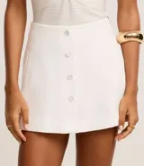 Short pollera de sastrería color blanco, con cintura alta y diseño de traspase frontal abotonado con botones forrados.