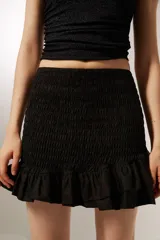 Minifalda negra de poliéster con frunces y volados en el ruedo.
