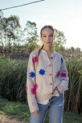 Cardigan tejido en lana color rosa claro con flores bordadas a mano en colores fucsia y azul. Tiene cuello redondo, cierre frontal con botones de madera y mangas largas.