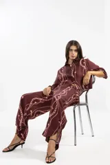 Camisa corta de lino color borgoña con estampado de cadenas y flores rosadas. Tiene cuello clásico, mangas largas y cierre frontal con botones.