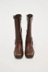 Bota de caña media color negro, estilo motociclista o cowboy, con puntera cuadrada y taco bajo. Presenta una tira ancha con hebillas metálicas alrededor del tobillo.