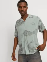Camisa de viscosa LENZING™ ECOVERO™ color verde con estampado de peces y olas en gris, cuello resort, mangas cortas y corte relajado.