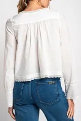 Blusa blanca de algodón con escote en U y mangas largas acampanadas. Presenta detalles de encaje en el escote, el frente y los puños.