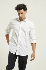 Camisa blanca de algodón premium, corte clásico, cuello inglés, cartera abotonada, mangas largas con puños ajustables y bajo redondeado.