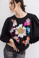 Buzo negro de algodón con cuello redondo y mangas largas abullonadas. Presenta apliques de flores bordadas con lentejuelas.