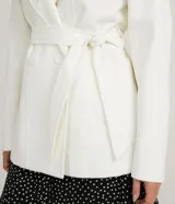 Campera alargada color blanco, confeccionada en polivelour, con cuello alto doblable, mangas largas, abotonado frontal doble, bolsillos y cinturón.