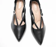 Zapato de tacón negro de charol con punta fina, tiras delgadas entrecruzadas sobre el empeine y hebilla plateada lateral. Tacón de bloque texturizado.