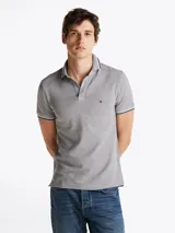Chomba gris de algodón elástico con cuello y mangas ribeteadas en blanco y negro. Tiene cartera de tres botones, logo de Tommy Hilfiger bordado en el pecho y corte slim.