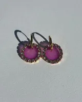 Aros colgantes con forma circular, hechos de resina color lila, con borde de strass plateado y arito de acero quirúrgico dorado.