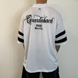 Remera negra estilo fútbol americano con cuello en V y mangas cortas con tres rayas blancas. Estampado frontal con logo y número 20 en blanco.