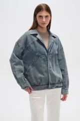 Campera de jean celeste con cuello clásico, solapas, cierre frontal con botones metálicos y mangas largas con puños abotonados. Presenta detalles de costuras diagonales y apliques de tachas metálicas.