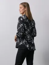 Blusa de gasa estampada con flores blancas sobre fondo negro, marca Floral & Ivy. Tiene cuello a la base con escote en V y mangas tres cuartos regulables con presilla y botón.