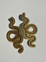 Par de aros colgantes con forma de serpiente dorada contorneada con strass y cierre a presión de acero inoxidable.