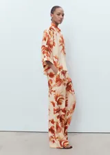 Pantalón de mujer de tejido fluido con estampado de palmeras en tonos naranja y beige. Diseño recto y largo, con tiro medio, dos bolsillos laterales y forro interior.