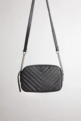 Cartera bandolera negra con diseño capitoneado en forma de V, correa de cuero y cadena plateada, cierre metálico y doble bolsillo interior.