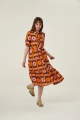 Vestido midi con estampado abstracto en tonos marrón, naranja y rosa. Tiene cuello camisero, mangas cortas abullonadas y falda escalonada con volantes.