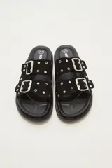 Sandalia tipo birkenstock de color negro, con dos tiras ajustables con hebillas metálicas plateadas. Las tiras están decoradas con tachas plateadas.