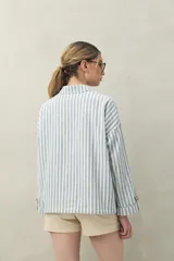 Chaqueta a rayas verticales celestes y blancas, con cuello camisero, cierre frontal con botones, dos bolsillos de parche en el pecho y mangas largas con puños abotonados.