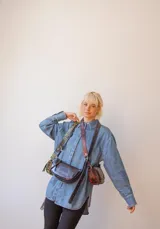 Bandolera de cuero color rojo con detalles en negro, con correa regulable y cierre superior con cremallera.