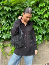 Camisa negra de tejido fino con detalles de cuero en los bolsillos y corte holgado.