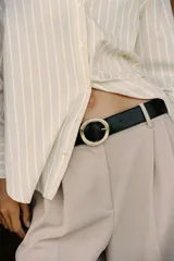Pantalón negro de tiro alto con pinzas delanteras, pernera ancha y cinturón con hebilla dorada.