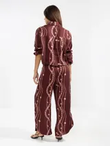 Pantalón de lino color marrón con estampado de cadenas en color rosa, de corte recto y talle medio, con cintura elástica solo por detrás, bolsillos delanteros y cortes redondeados a los costados.